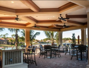 photo of outdoor dining area at a southwest Florida club, bar, tables and chairs arranged under a coffered ceiling with a view of a lake surrounded by palm trees