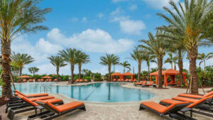 Seagate Development Esplanade Lake Club view of a swimming pool surrounded by green palm trees and bright range chaise lounges.